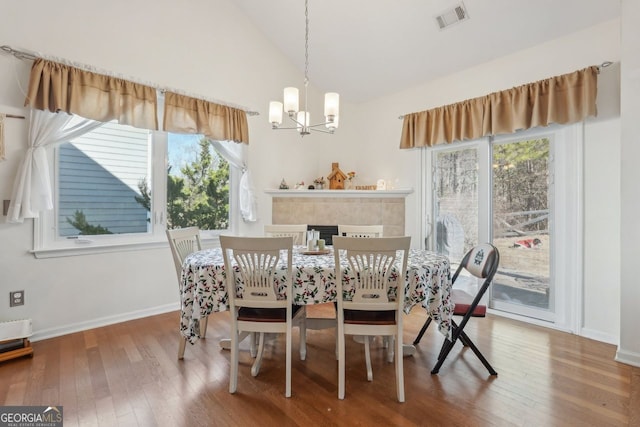 dining room featuring vaulted ceiling, a chandelier, a fireplace, and hardwood / wood-style floors