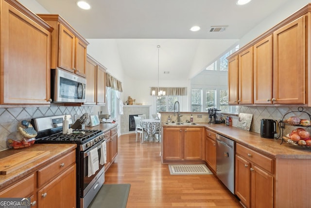 kitchen featuring stainless steel appliances, tasteful backsplash, light hardwood / wood-style floors, sink, and hanging light fixtures