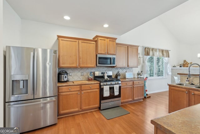 kitchen featuring appliances with stainless steel finishes, tasteful backsplash, light wood-type flooring, lofted ceiling, and sink