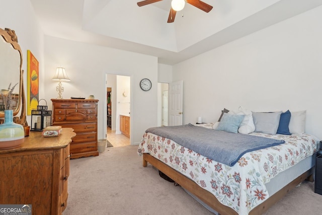 bedroom with ceiling fan, connected bathroom, a tray ceiling, and light carpet