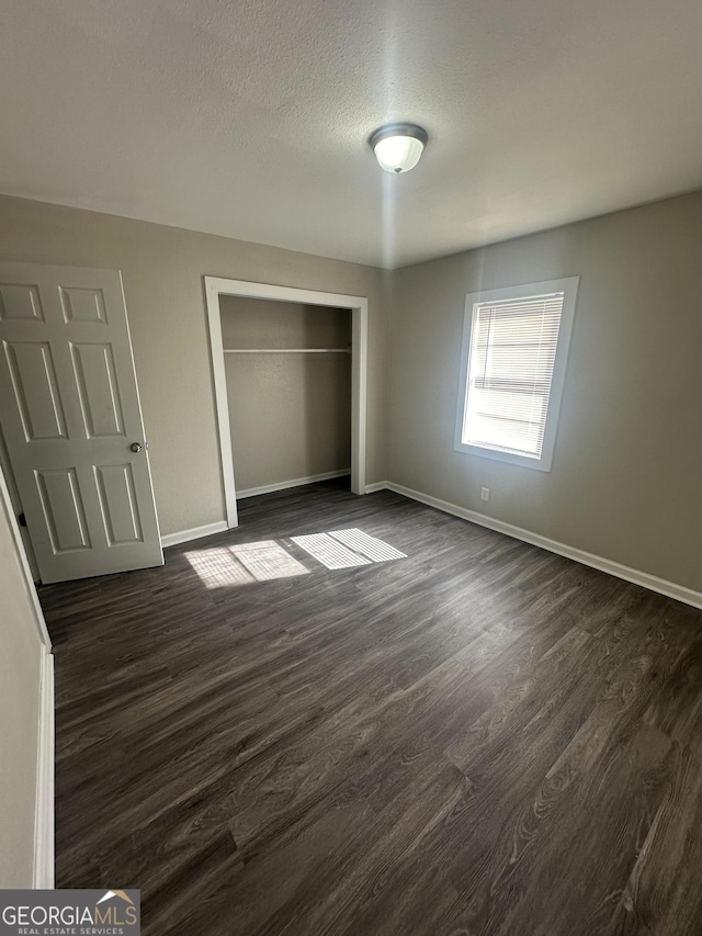 unfurnished bedroom with a textured ceiling, dark hardwood / wood-style floors, and a closet