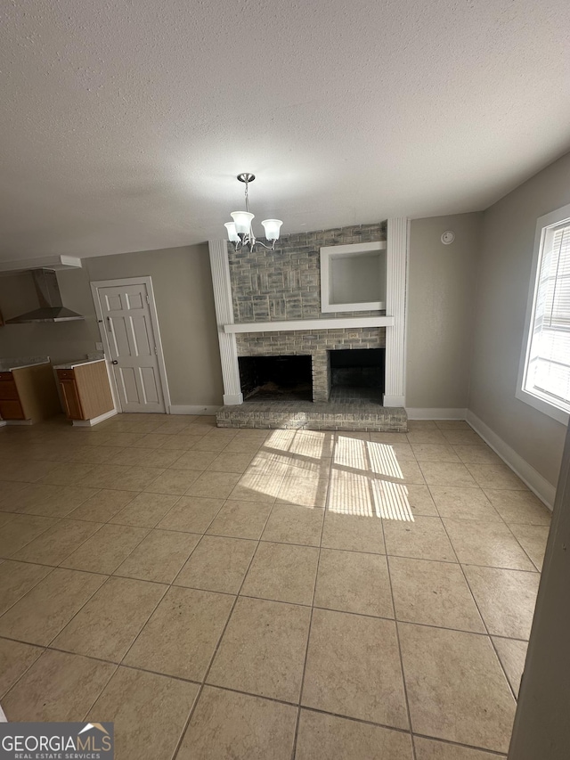 unfurnished living room featuring a chandelier, light tile patterned floors, a textured ceiling, and a brick fireplace