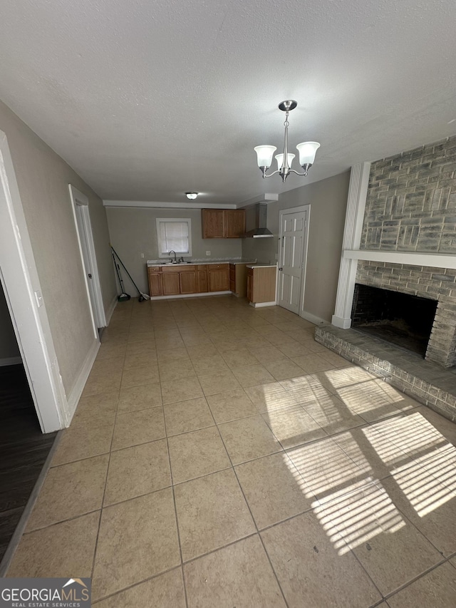 unfurnished living room featuring a brick fireplace, a textured ceiling, sink, a chandelier, and light tile patterned flooring