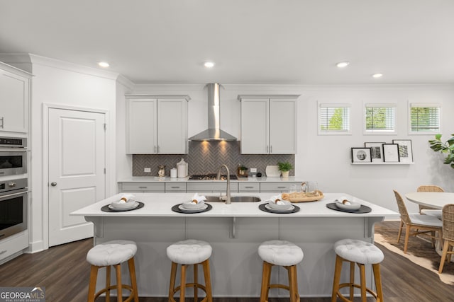 kitchen with white cabinetry, a kitchen island with sink, wall chimney exhaust hood, and sink