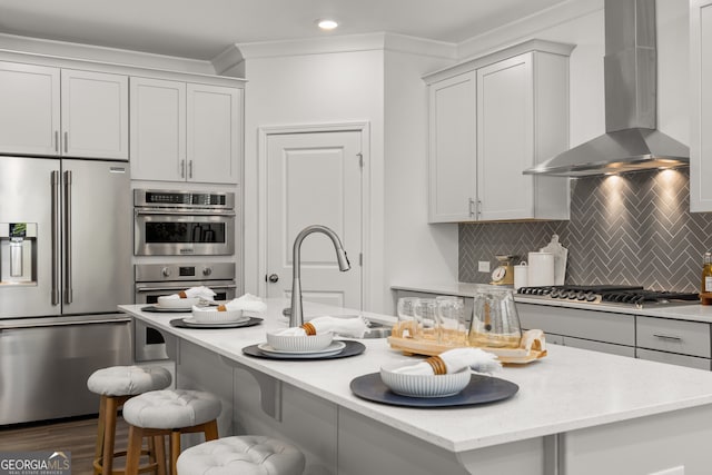 kitchen featuring decorative backsplash, appliances with stainless steel finishes, a kitchen island with sink, and wall chimney range hood