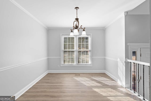 unfurnished dining area featuring light wood-type flooring, an inviting chandelier, and crown molding