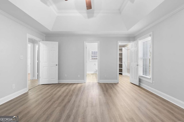 unfurnished bedroom with ceiling fan, a raised ceiling, a spacious closet, and ensuite bathroom