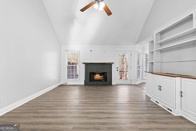 unfurnished living room featuring ceiling fan, dark hardwood / wood-style floors, high vaulted ceiling, and built in shelves