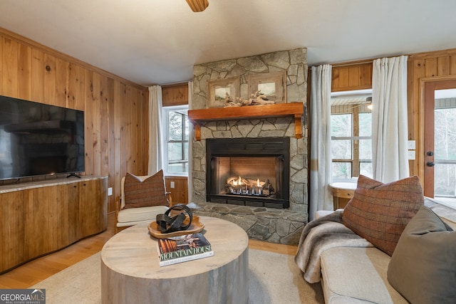 living room with a stone fireplace, wooden walls, a wealth of natural light, and light wood-type flooring