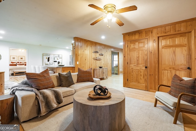 living room with wood walls, ceiling fan, and light hardwood / wood-style floors