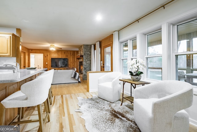 living room with wooden walls, light hardwood / wood-style flooring, ceiling fan, and sink