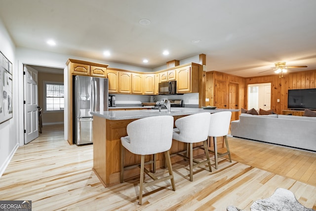 kitchen featuring a kitchen bar, stainless steel fridge, ceiling fan, wooden walls, and light hardwood / wood-style flooring