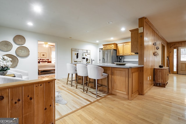 kitchen featuring a breakfast bar, wood walls, stainless steel fridge, light hardwood / wood-style floors, and kitchen peninsula