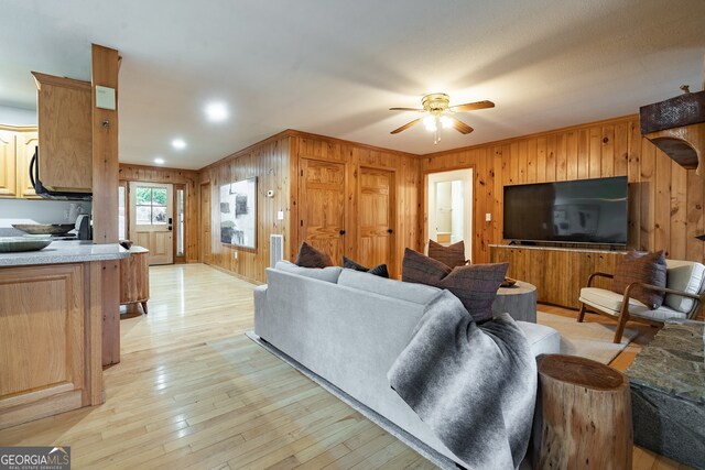 living room featuring ceiling fan, wood walls, and light hardwood / wood-style flooring