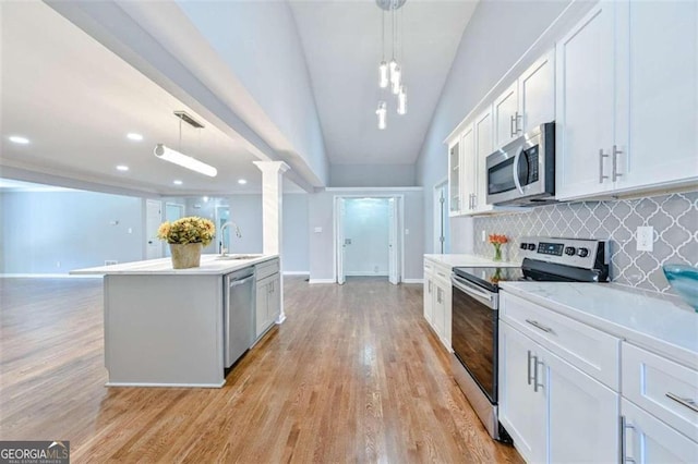 kitchen featuring white cabinetry, stainless steel appliances, tasteful backsplash, lofted ceiling, and decorative light fixtures