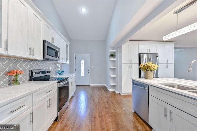 kitchen featuring white cabinetry, sink, stainless steel appliances, vaulted ceiling, and decorative light fixtures