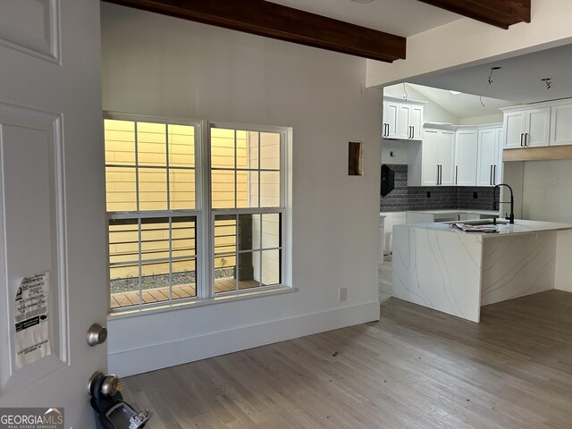 kitchen featuring beam ceiling, light hardwood / wood-style flooring, white cabinetry, and sink