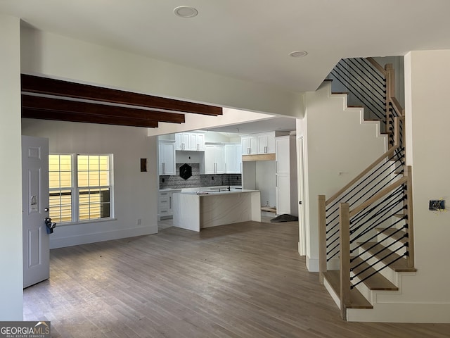 kitchen with backsplash, beam ceiling, white cabinets, a center island, and light hardwood / wood-style floors