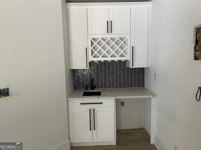 bar featuring sink, light stone countertops, white cabinetry, and backsplash