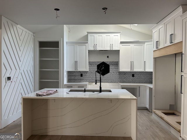 kitchen with a kitchen island with sink, sink, vaulted ceiling, decorative backsplash, and white cabinetry