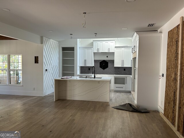 kitchen with a kitchen island with sink, sink, decorative backsplash, light wood-type flooring, and white cabinetry