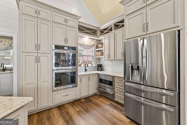 kitchen featuring vaulted ceiling, sink, appliances with stainless steel finishes, dark hardwood / wood-style flooring, and light stone counters