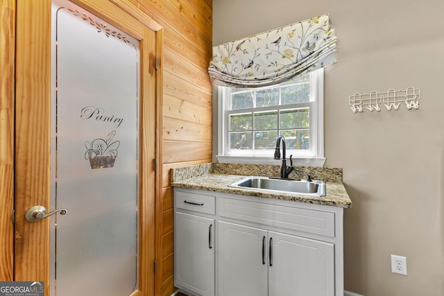 kitchen with light stone counters, sink, white cabinetry, and wood walls