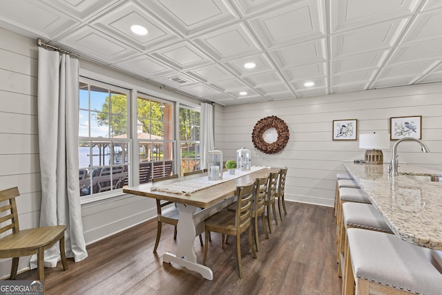 dining room featuring dark wood-type flooring, sink, wood walls, and a water view