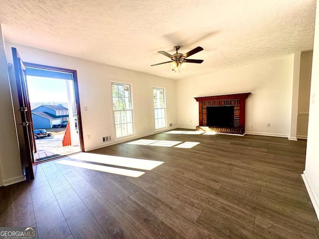 unfurnished living room featuring a textured ceiling, dark hardwood / wood-style flooring, a brick fireplace, and ceiling fan