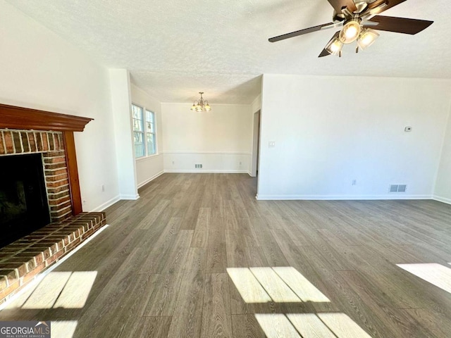 unfurnished living room featuring ceiling fan with notable chandelier, dark hardwood / wood-style flooring, a textured ceiling, and a brick fireplace