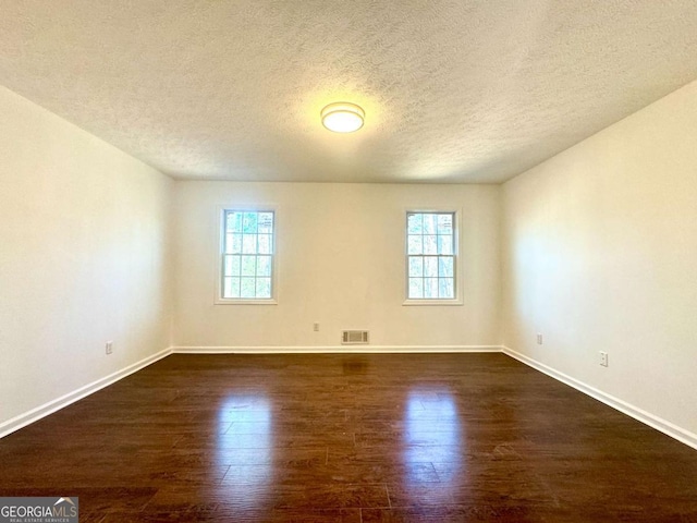 empty room with plenty of natural light, dark hardwood / wood-style flooring, and a textured ceiling