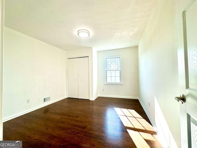 unfurnished bedroom with a textured ceiling, a closet, and dark hardwood / wood-style floors