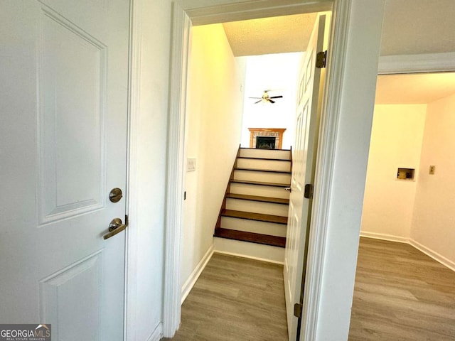 staircase featuring ceiling fan, hardwood / wood-style floors, and a brick fireplace