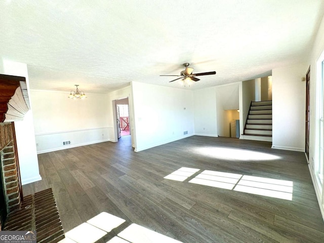 unfurnished living room featuring a textured ceiling, dark hardwood / wood-style floors, a fireplace, and ceiling fan with notable chandelier