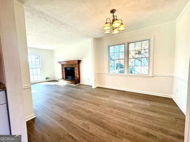 unfurnished living room featuring a brick fireplace, dark hardwood / wood-style flooring, a textured ceiling, and an inviting chandelier