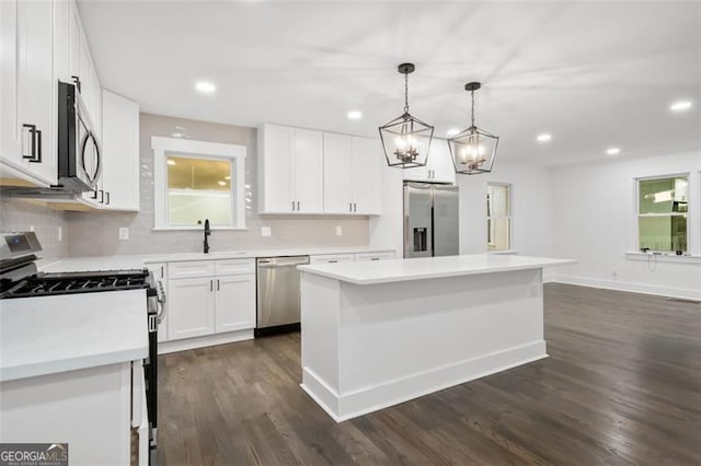 kitchen featuring white cabinetry, dark wood-type flooring, stainless steel appliances, decorative light fixtures, and a kitchen island