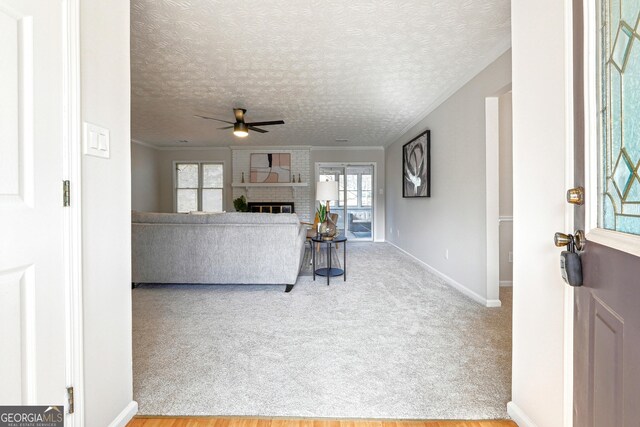 living room with carpet, crown molding, ceiling fan, a fireplace, and a textured ceiling