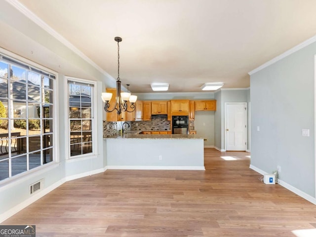 kitchen featuring sink, tasteful backsplash, kitchen peninsula, pendant lighting, and a chandelier