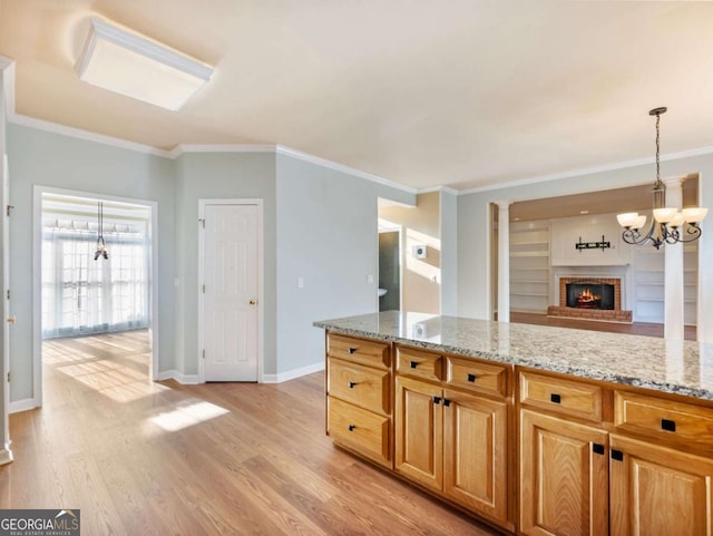 kitchen featuring crown molding, light wood-type flooring, a fireplace, light stone countertops, and a notable chandelier