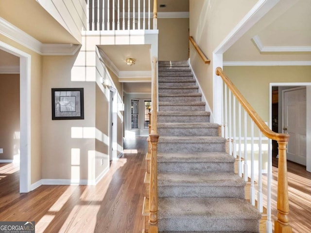 stairs featuring wood-type flooring, a towering ceiling, and ornamental molding