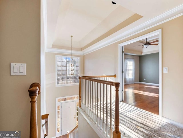 hall with a chandelier, wood-type flooring, crown molding, and a tray ceiling