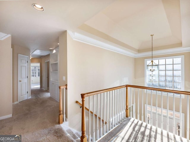 corridor featuring carpet, an inviting chandelier, ornamental molding, and a tray ceiling