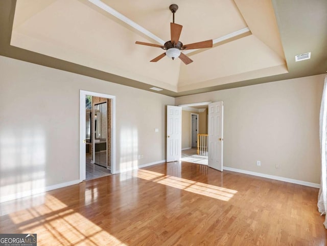 unfurnished room with a high ceiling, light wood-type flooring, a raised ceiling, and ceiling fan