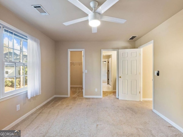 unfurnished bedroom featuring ceiling fan, a walk in closet, light carpet, and a closet