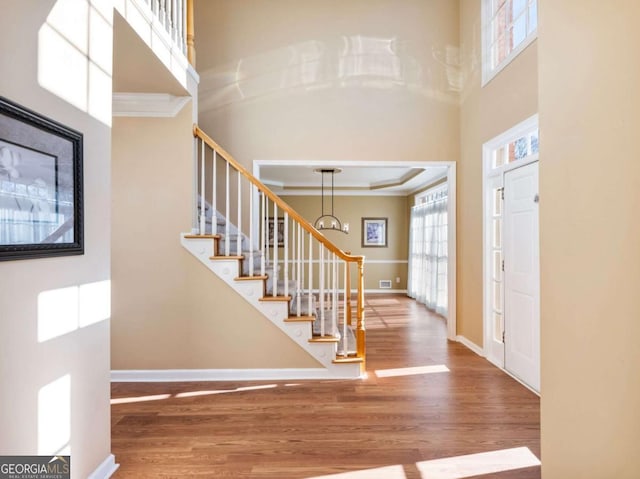 entryway featuring hardwood / wood-style floors, a notable chandelier, crown molding, and a high ceiling