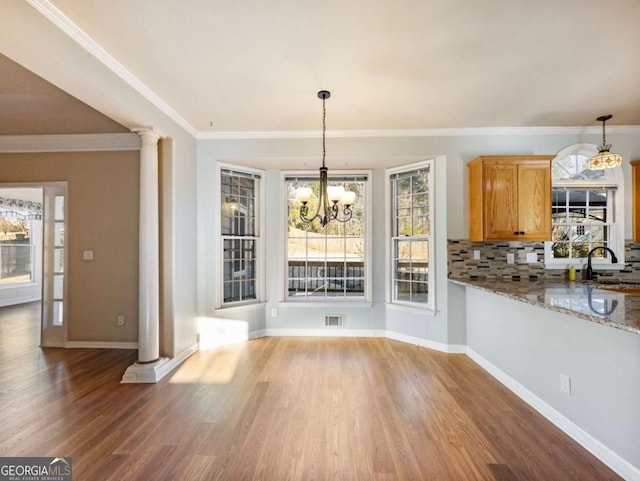 unfurnished dining area with hardwood / wood-style floors, an inviting chandelier, sink, ornate columns, and ornamental molding