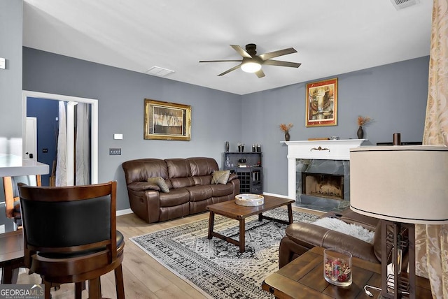 living room with a high end fireplace, light hardwood / wood-style flooring, and ceiling fan