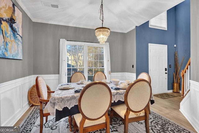 dining area with light hardwood / wood-style floors, ornamental molding, a wealth of natural light, and an inviting chandelier