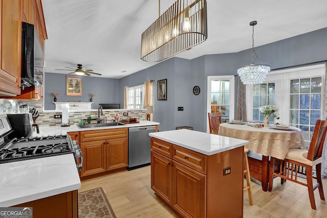 kitchen with sink, stainless steel appliances, pendant lighting, a kitchen island, and ceiling fan with notable chandelier