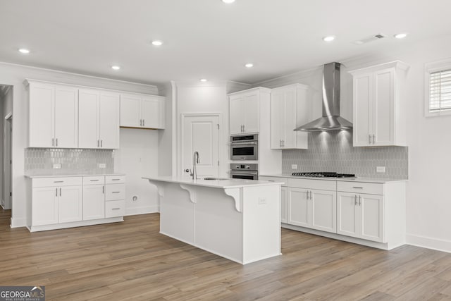 kitchen featuring white cabinetry, sink, wall chimney exhaust hood, a kitchen island with sink, and light wood-type flooring